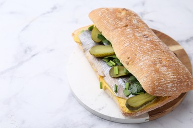 Tasty sandwich with herring, pickles, green onions and parsley on white marble table, closeup. Space for text