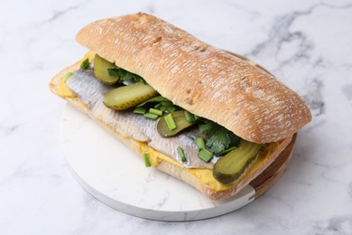 Tasty sandwich with herring, pickles, green onions and parsley on white marble table, closeup