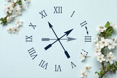 Image of Clock and blossoming branches with white flowers on light blue background, top view. Arrow showing time change one hour ahead in spring. Daylight saving time