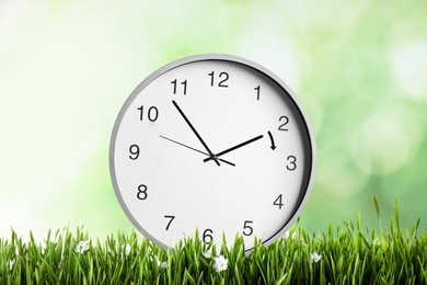 Image of Clock in green grass with flowers. Arrow showing time change one hour ahead in spring. Daylight saving time