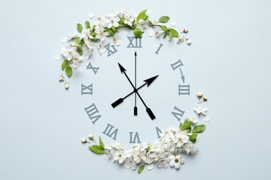 Image of Clock and white flowers on light blue background, top view. Arrow showing time change one hour ahead in spring. Daylight saving time