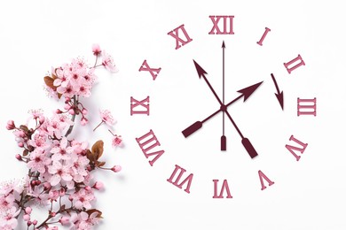 Image of Clock and blossoming branch with pink flowers on white background, top view. Arrow showing time change one hour ahead in spring. Daylight saving time