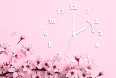 Image of Clock and blossoming branch with flowers on pink background, top view. Arrow showing time change one hour ahead in spring. Daylight saving time