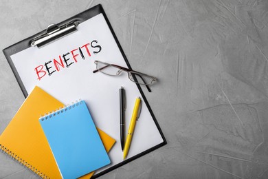 Paper with word Benefits, clipboard, eyeglasses, notebook and pens on grey table, top view. Space for text