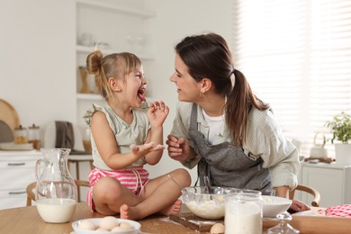 Photo of Little girl helping her mom making dough at table in kitchen