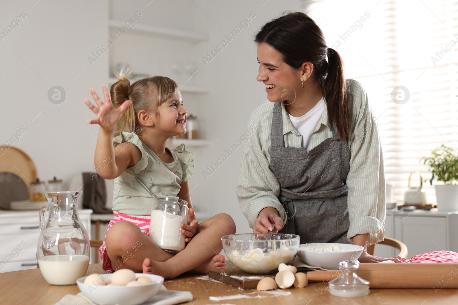 Photo of Little girl helping her mom making dough at table in kitchen