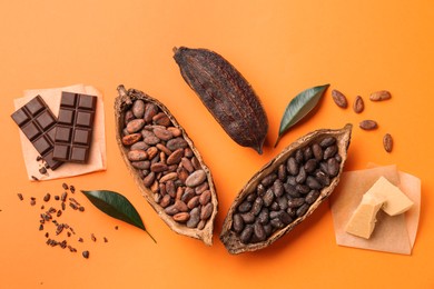 Photo of Cocoa pods with beans, chocolate and butter on orange background, flat lay