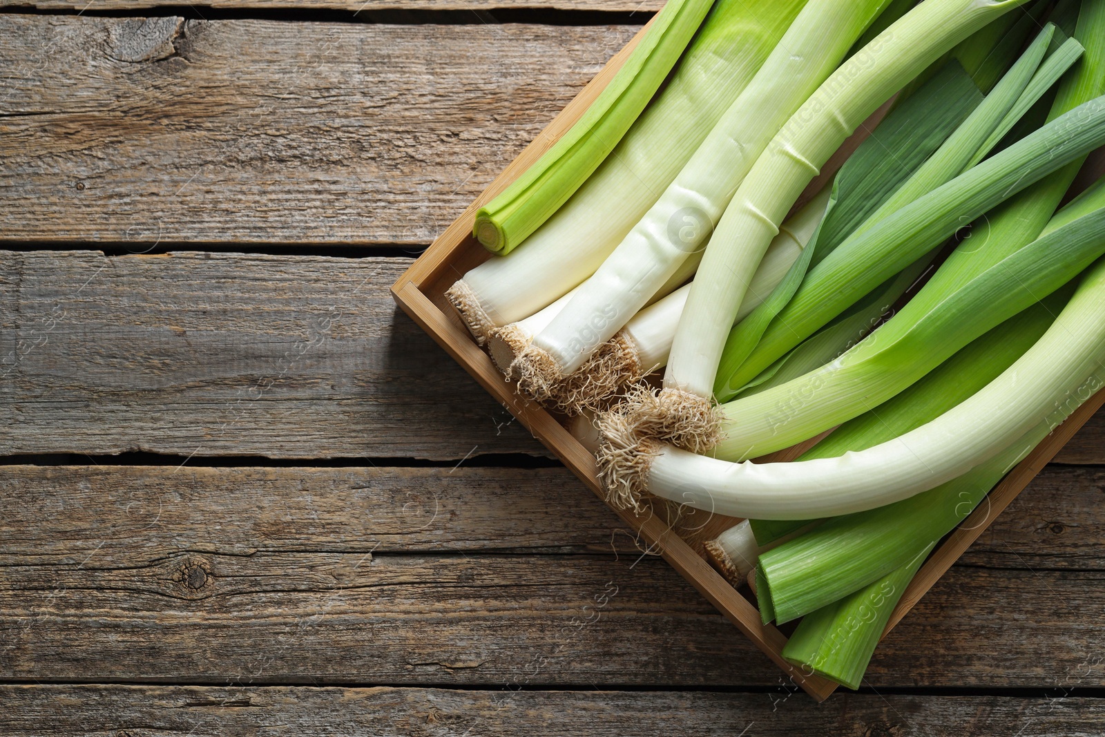 Photo of Fresh leeks in crate on wooden table, top view. Space for text