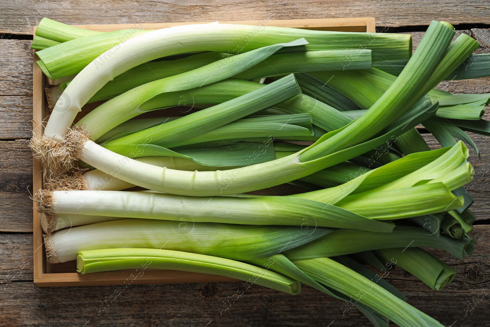 Photo of Fresh leeks in crate on wooden table, top view