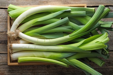 Photo of Fresh leeks in crate on wooden table, top view