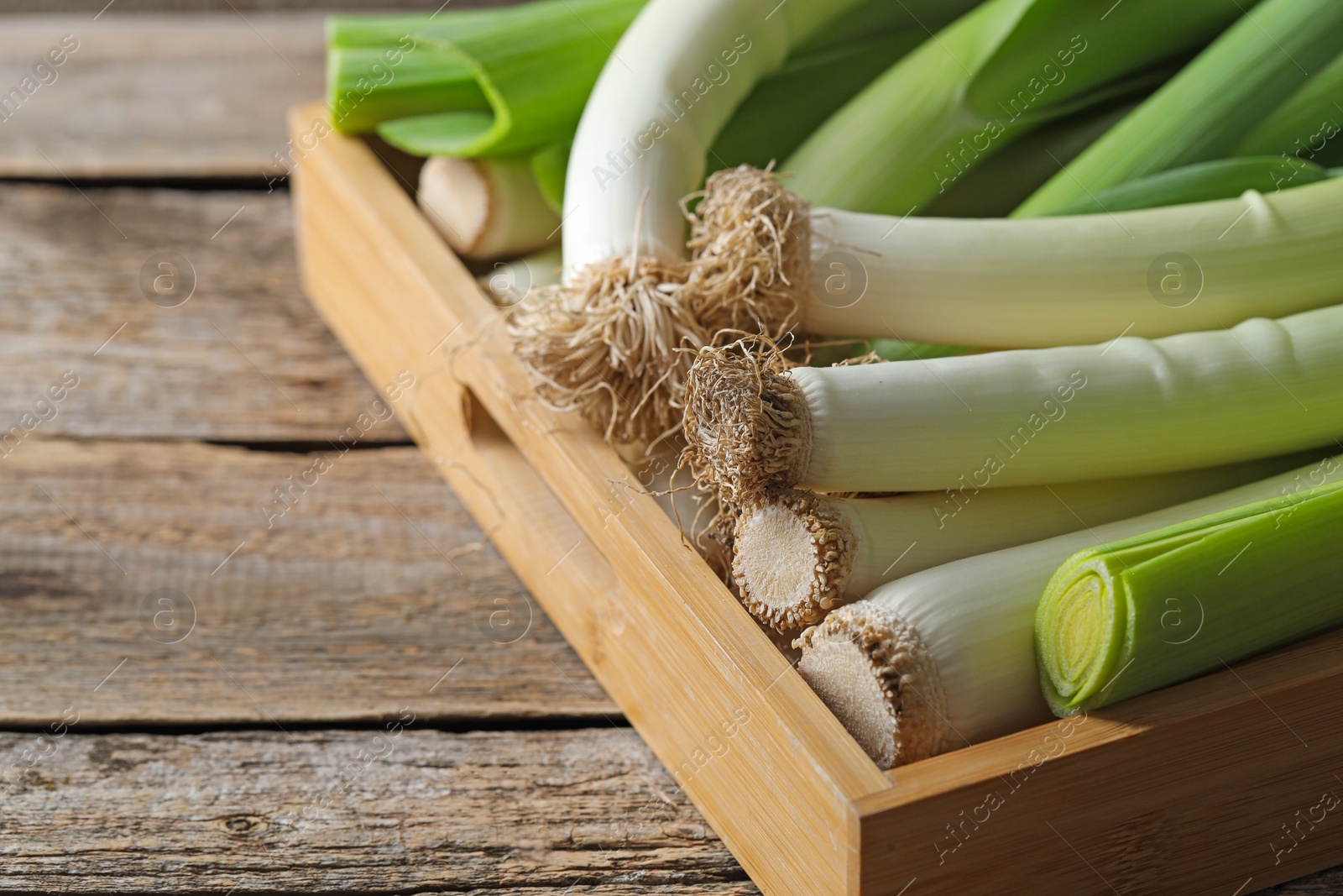 Photo of Fresh leeks in crate on wooden table, closeup