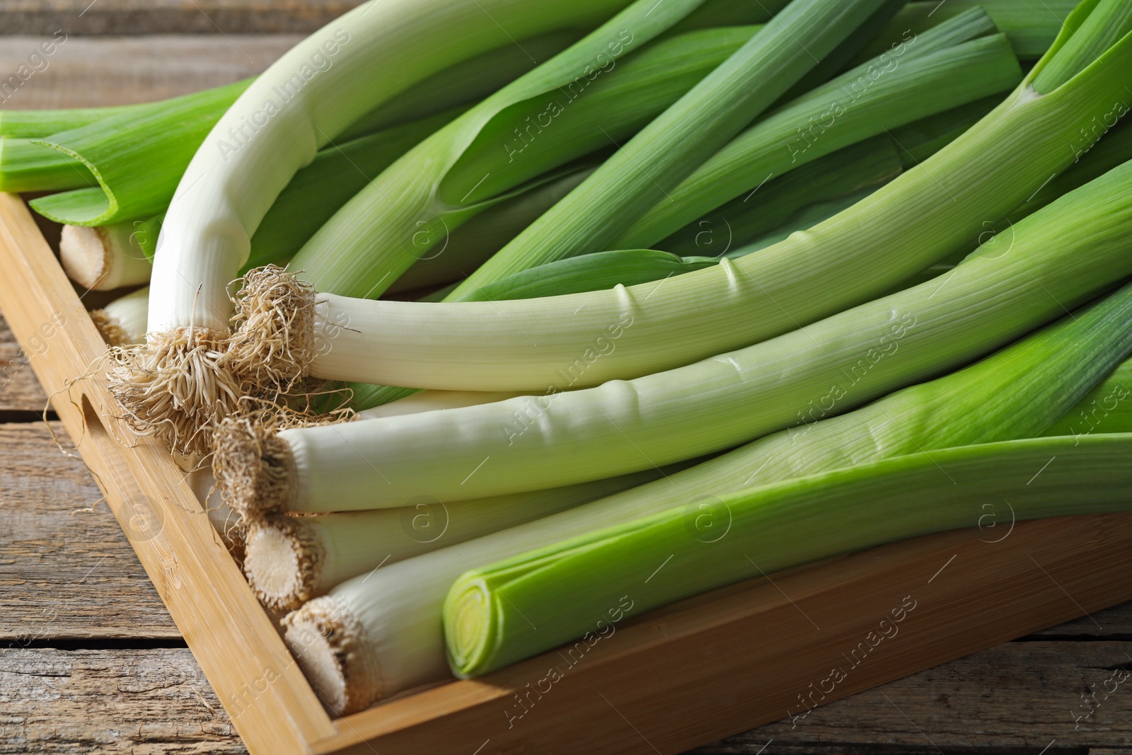 Photo of Fresh leeks in crate on wooden table, closeup