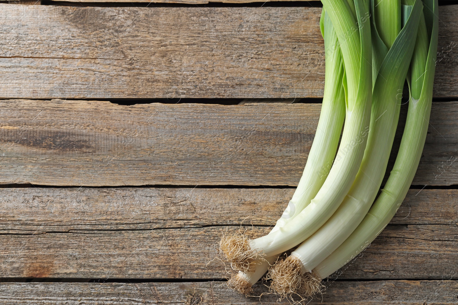 Photo of Whole fresh leeks on wooden table, top view. Space for text