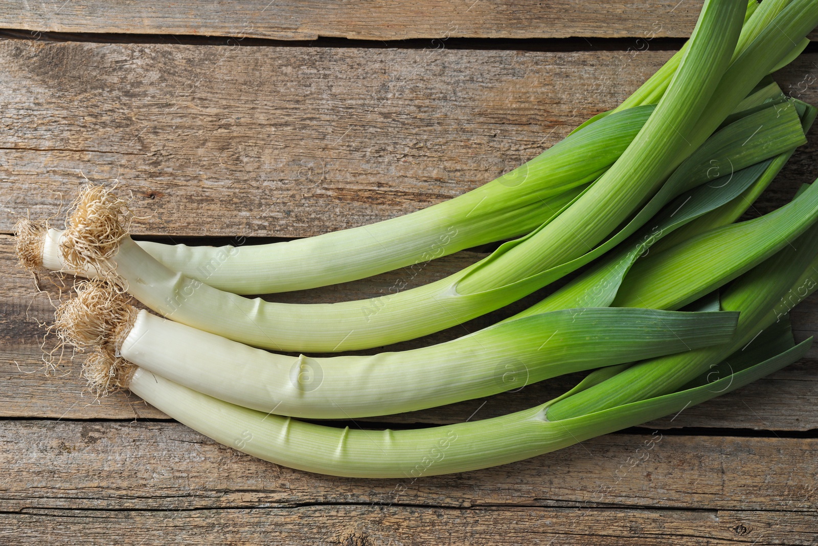 Photo of Whole fresh leeks on wooden table, top view