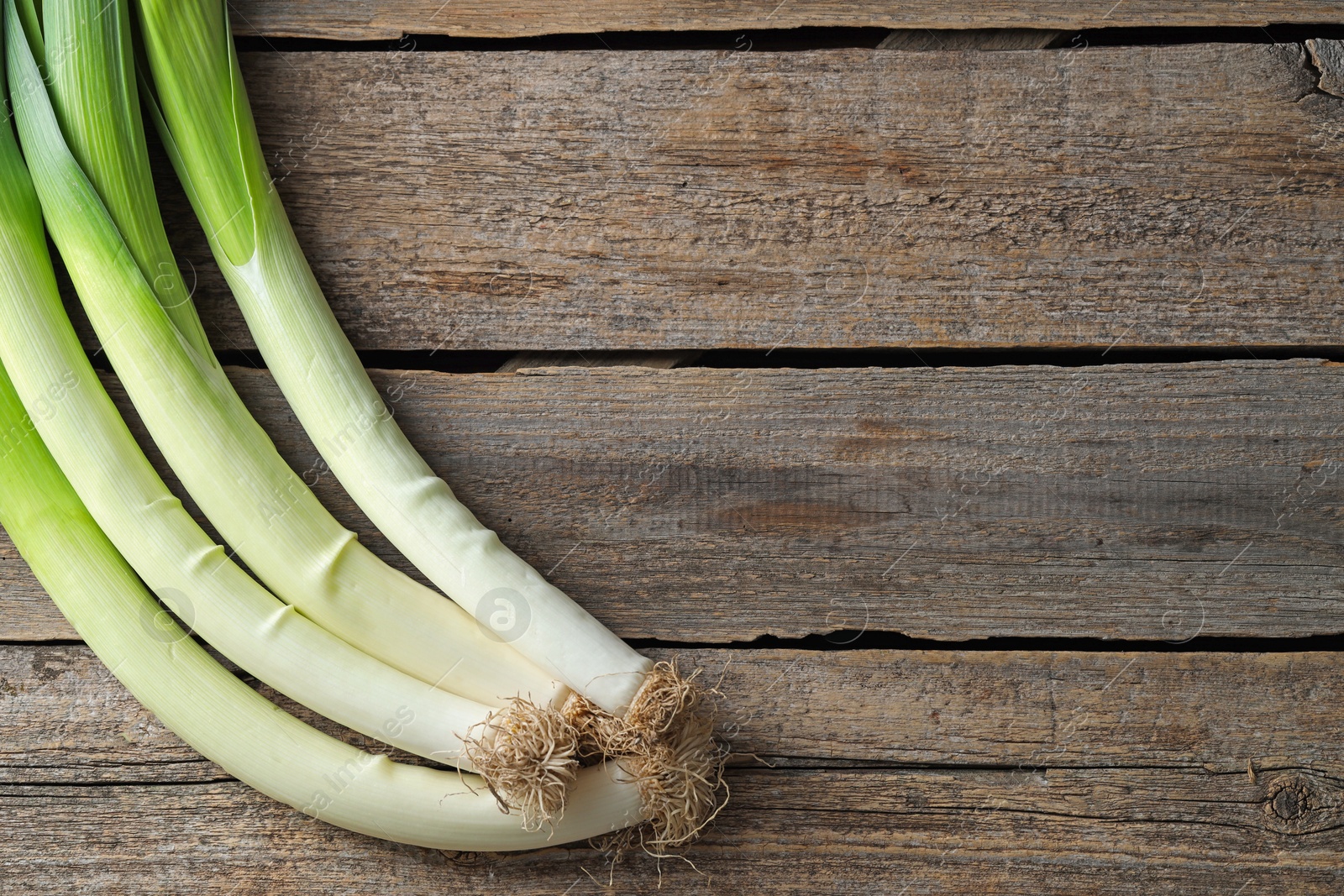 Photo of Whole fresh leeks on wooden table, top view. Space for text