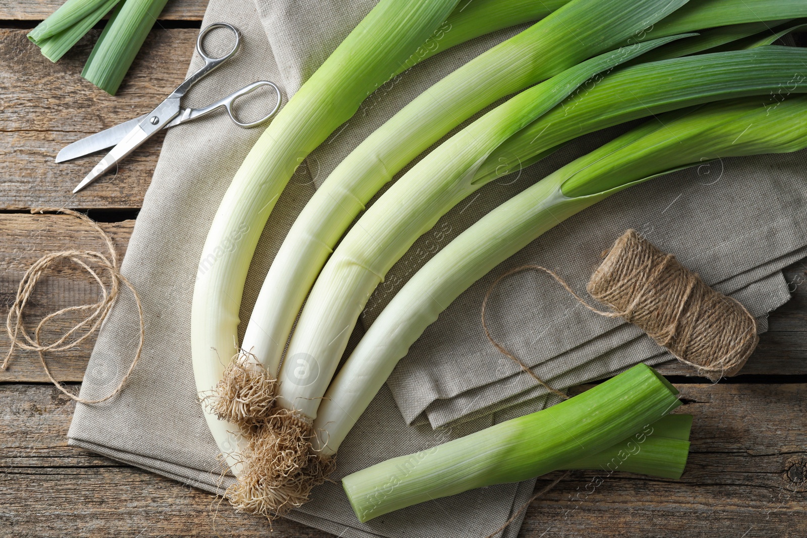 Photo of Whole fresh leeks, thread, scissors and towel on wooden table, flat lay