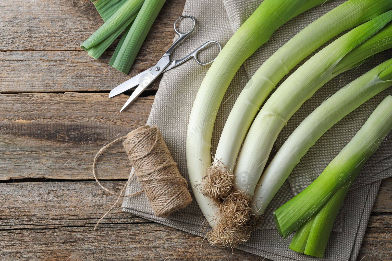 Photo of Whole fresh leeks, thread, scissors and towel on wooden table, flat lay