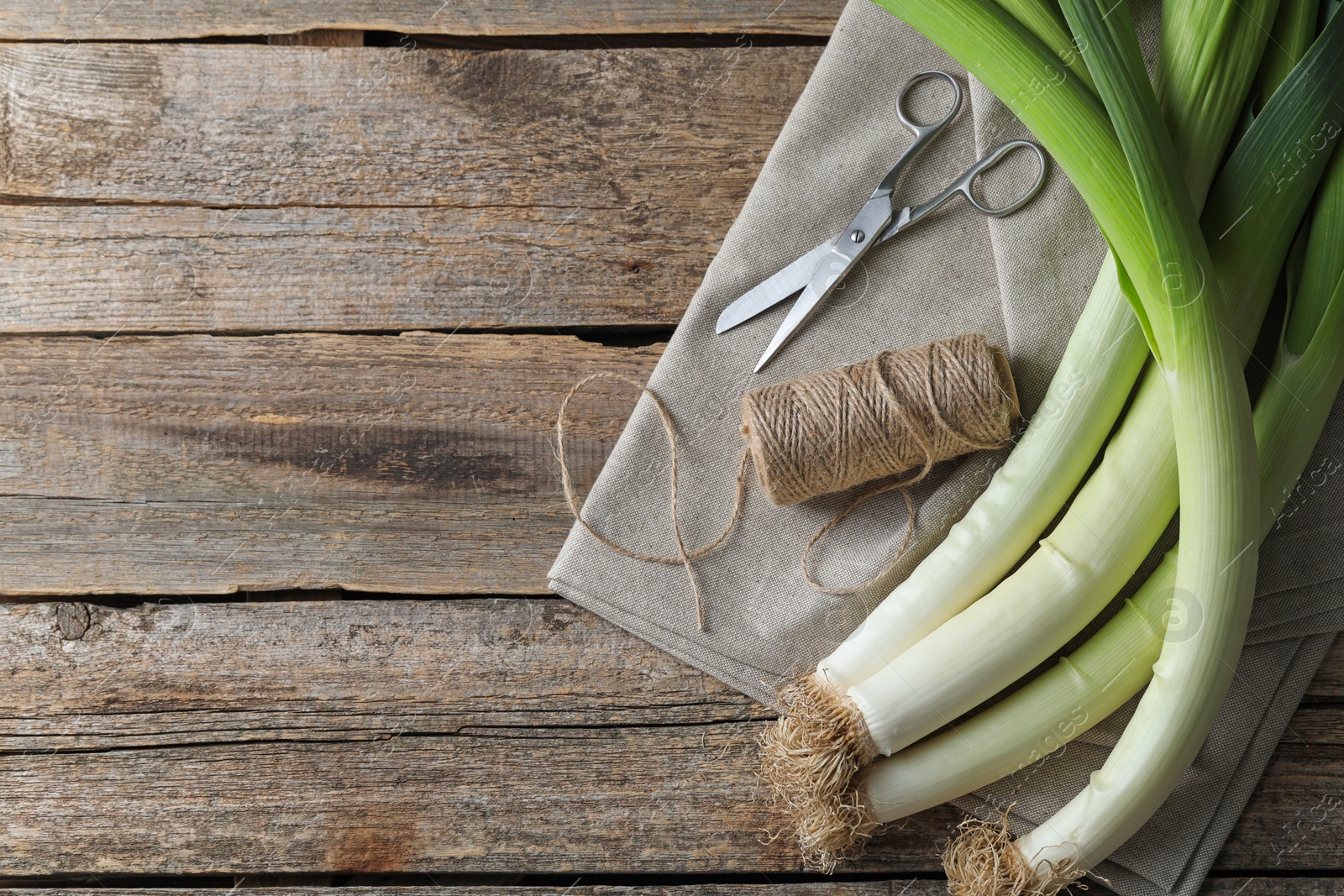 Photo of Whole fresh leeks, thread, scissors and towel on wooden table, flat lay. Space for text