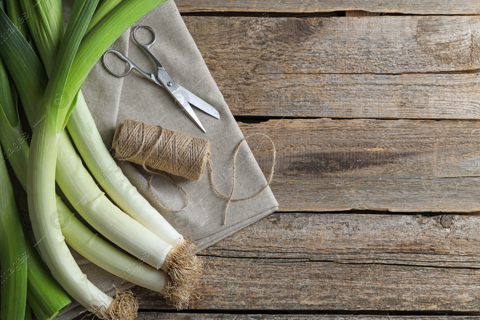 Photo of Whole fresh leeks, thread, scissors and towel on wooden table, flat lay. Space for text