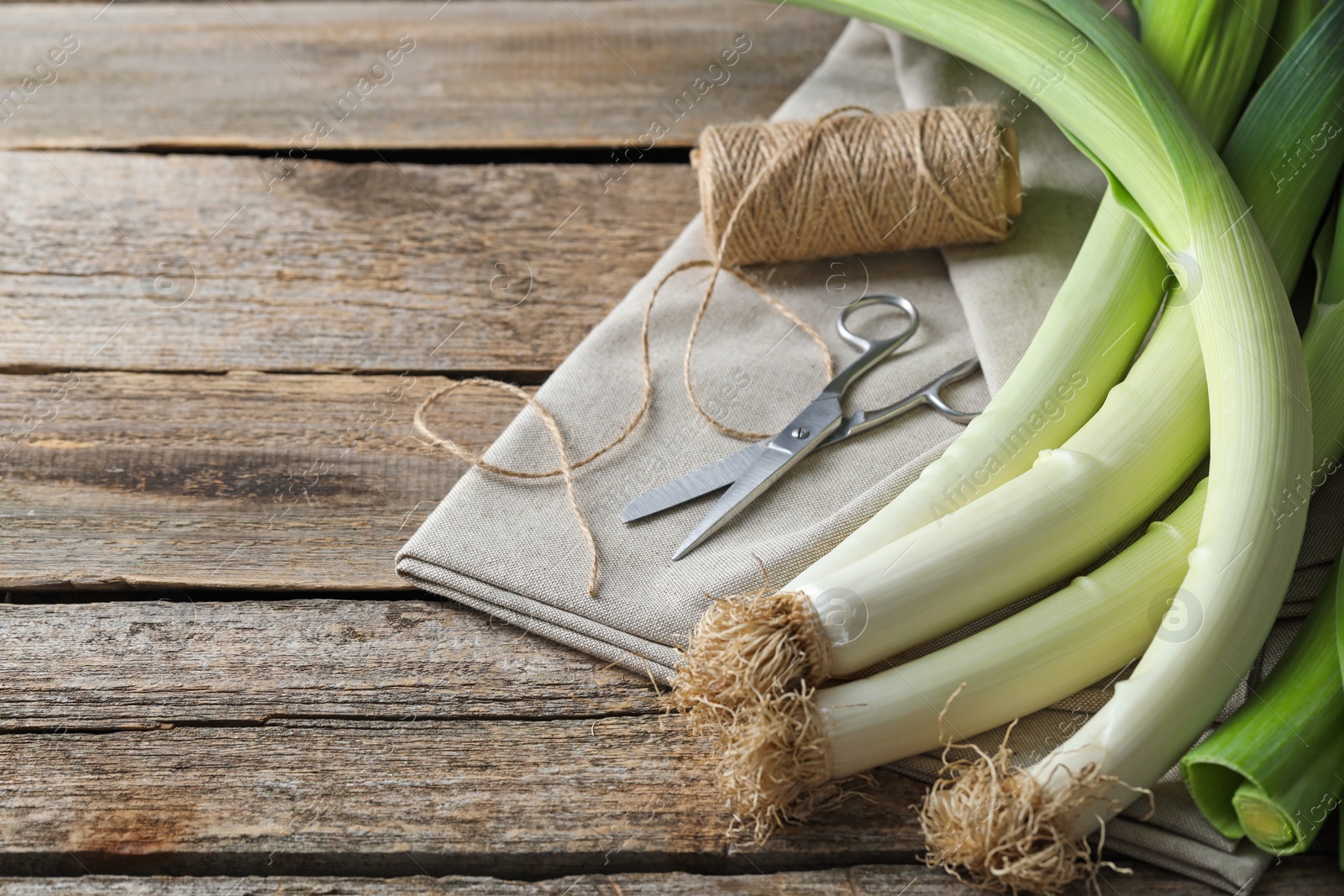 Photo of Whole fresh leeks, thread, scissors and towel on wooden table, closeup. Space for text