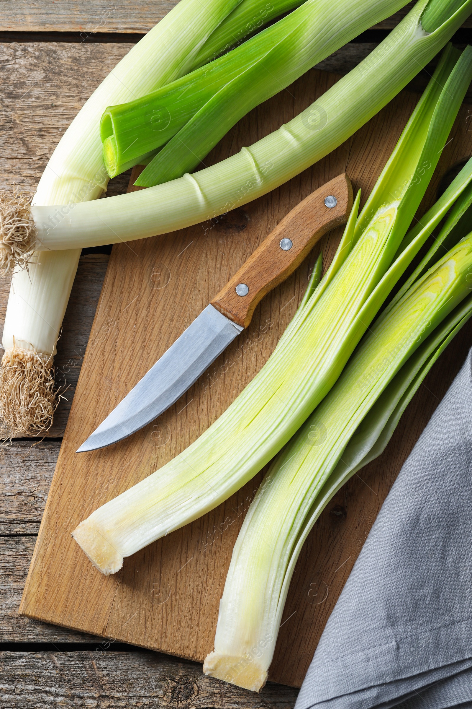 Photo of Whole fresh leeks, knife and towel on wooden table, top view