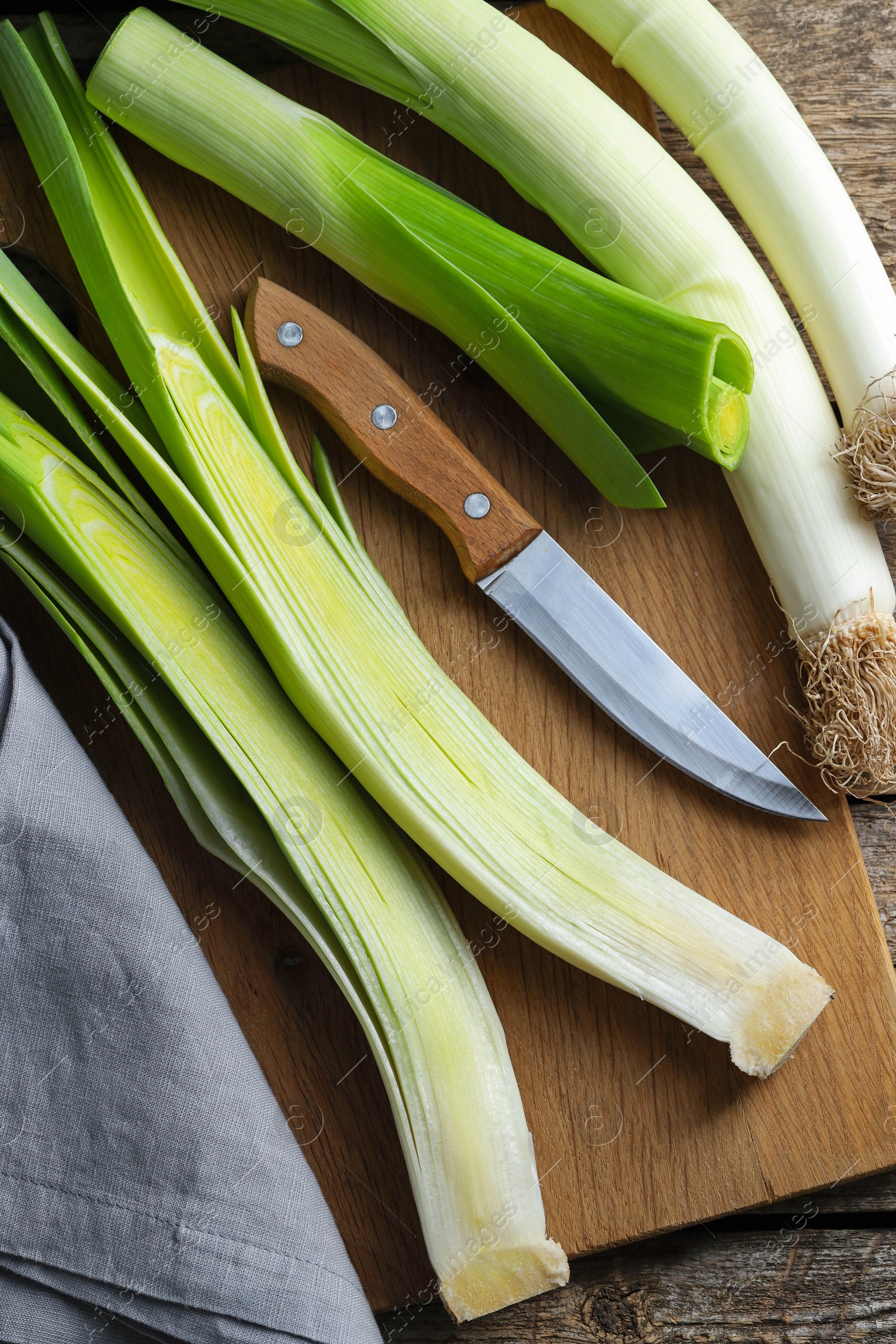 Photo of Whole fresh leeks, knife and towel on wooden table, top view