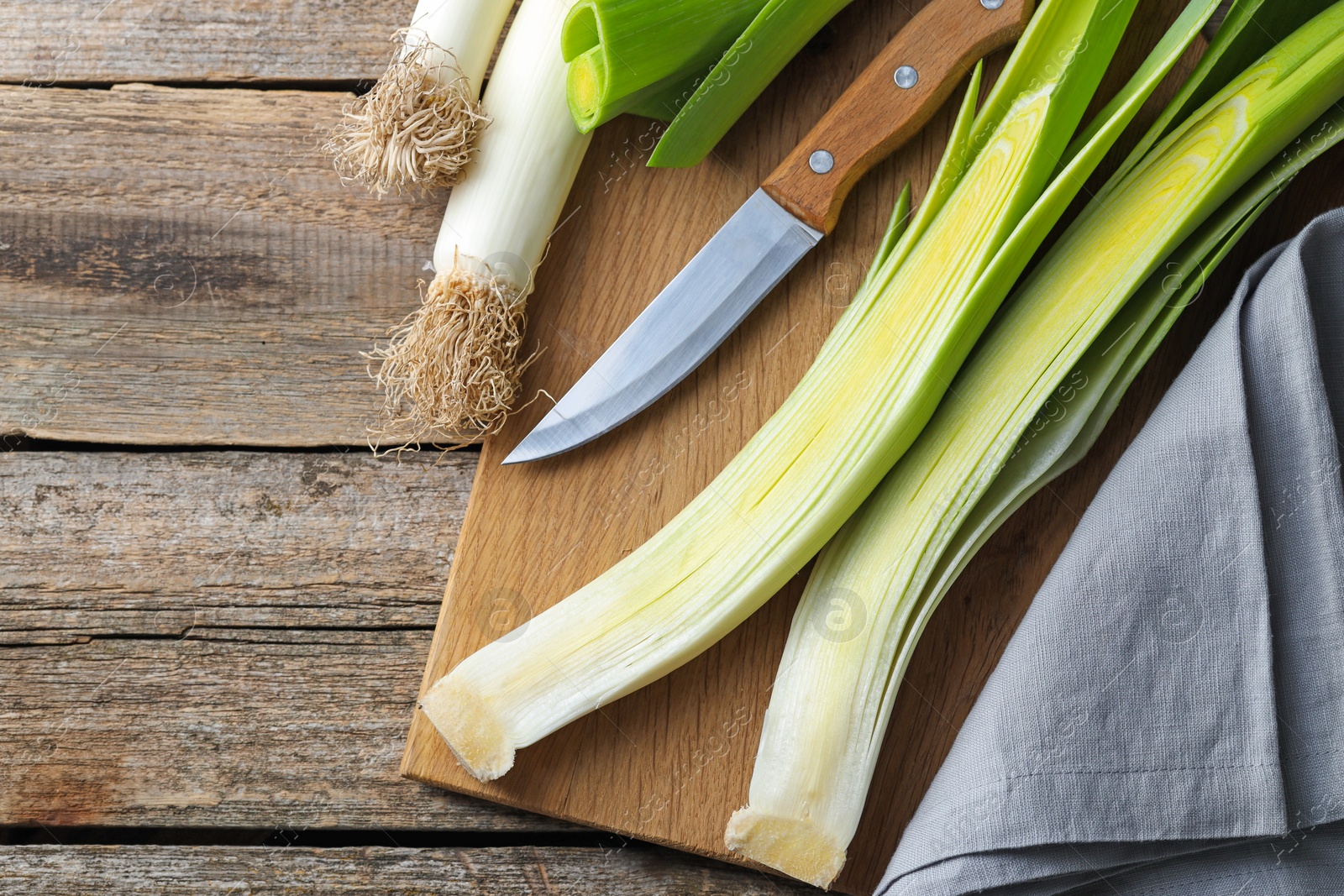 Photo of Whole fresh leeks, knife and towel on wooden table, top view