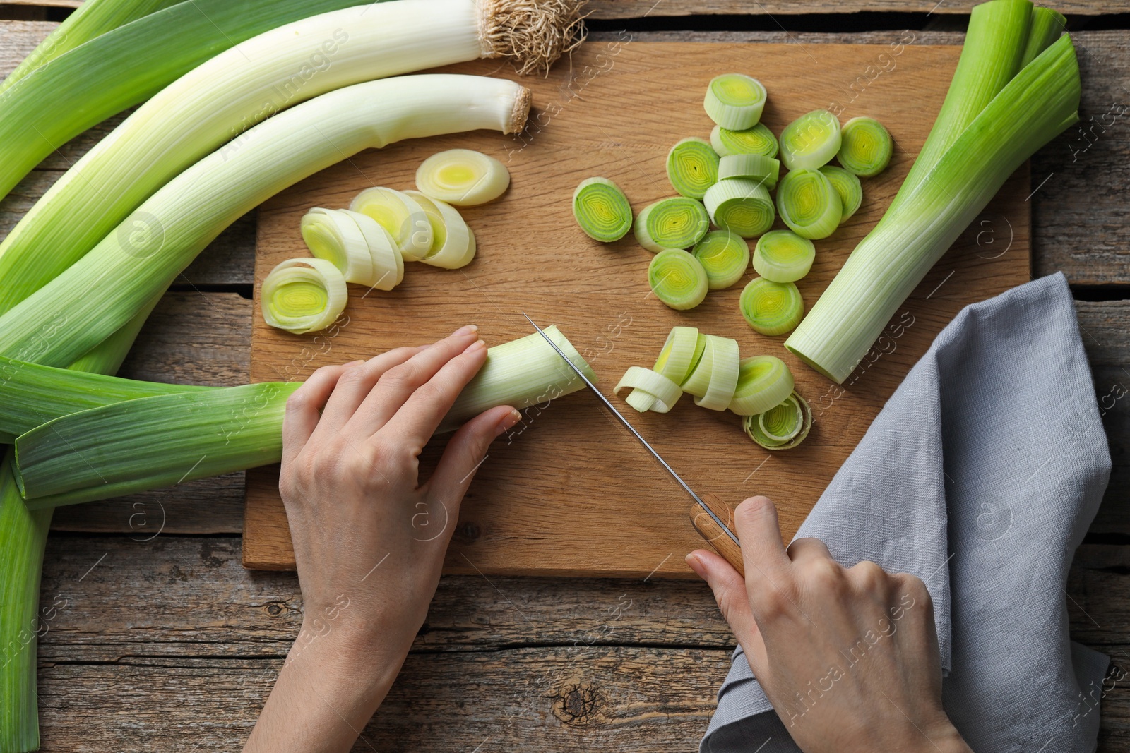 Photo of Woman cutting fresh leek at wooden table, top view