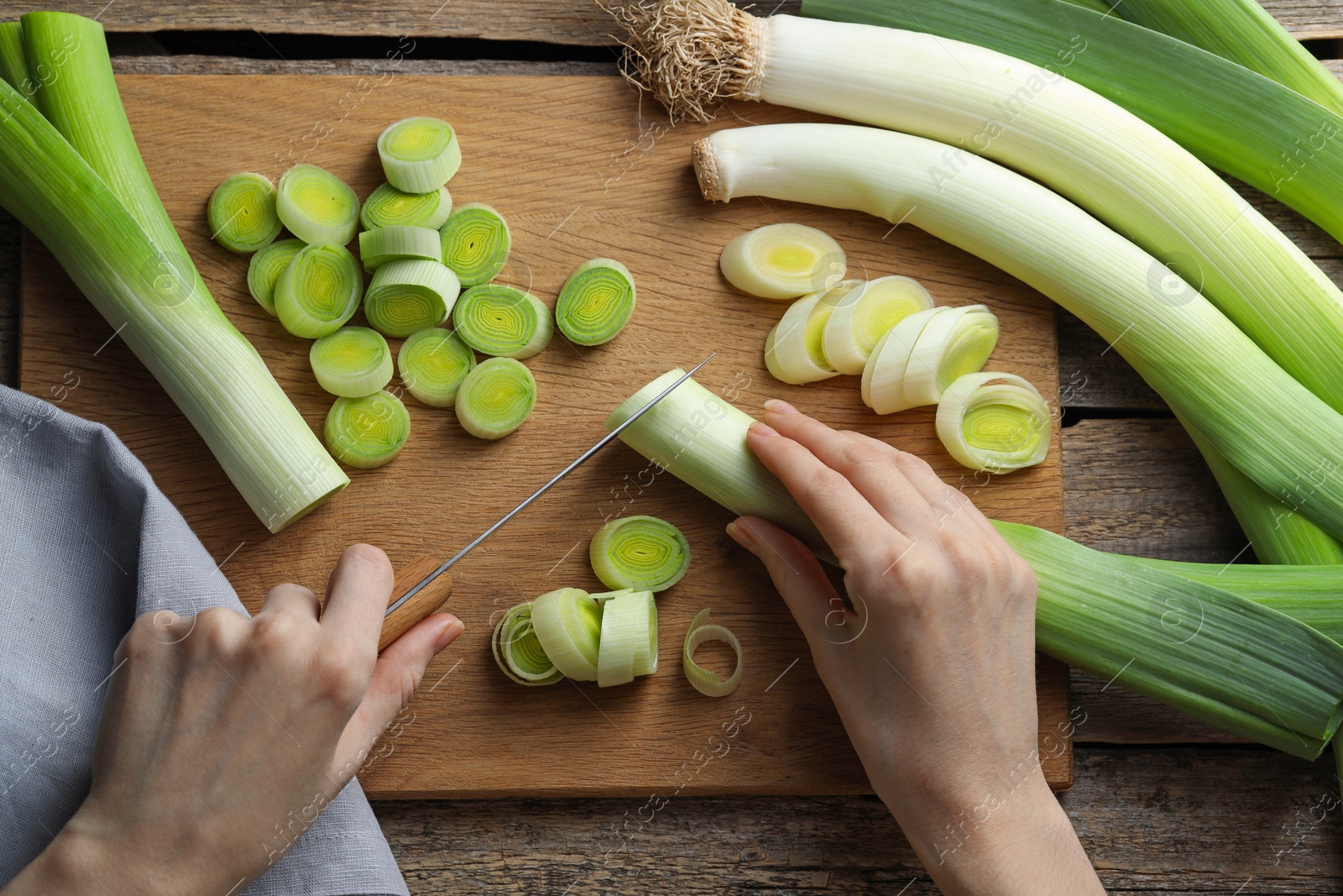 Photo of Woman cutting fresh leek at wooden table, top view