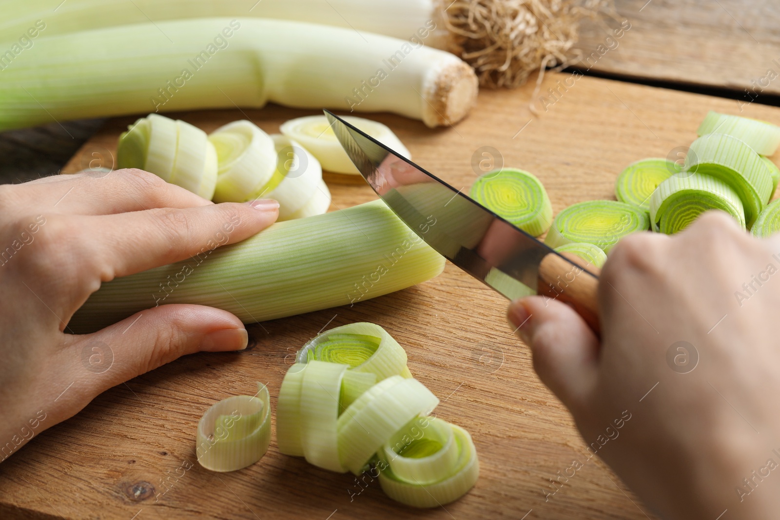 Photo of Woman cutting fresh leek at wooden table, closeup