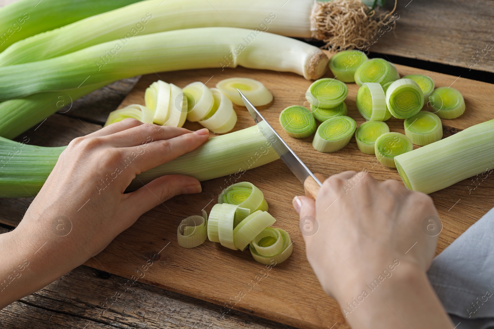 Photo of Woman cutting fresh leek at wooden table, closeup