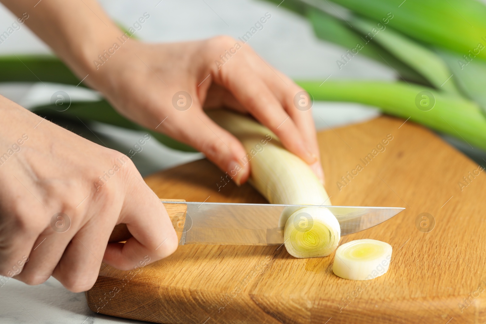 Photo of Woman cutting fresh leek at white table, closeup