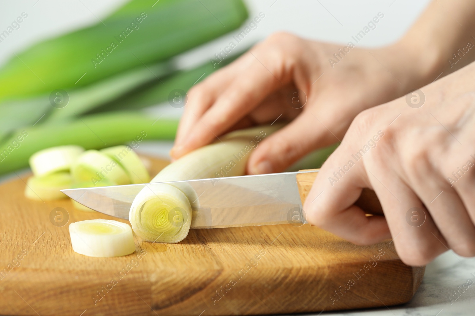 Photo of Woman cutting fresh leek at white table, closeup