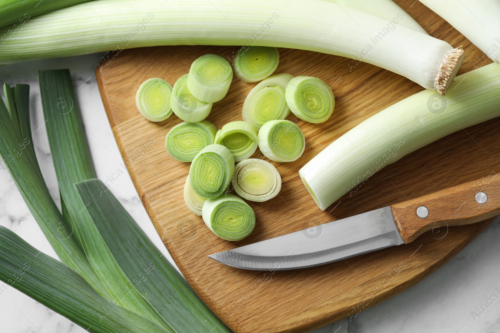 Photo of Chopped leeks, knife and board on white table, flat lay