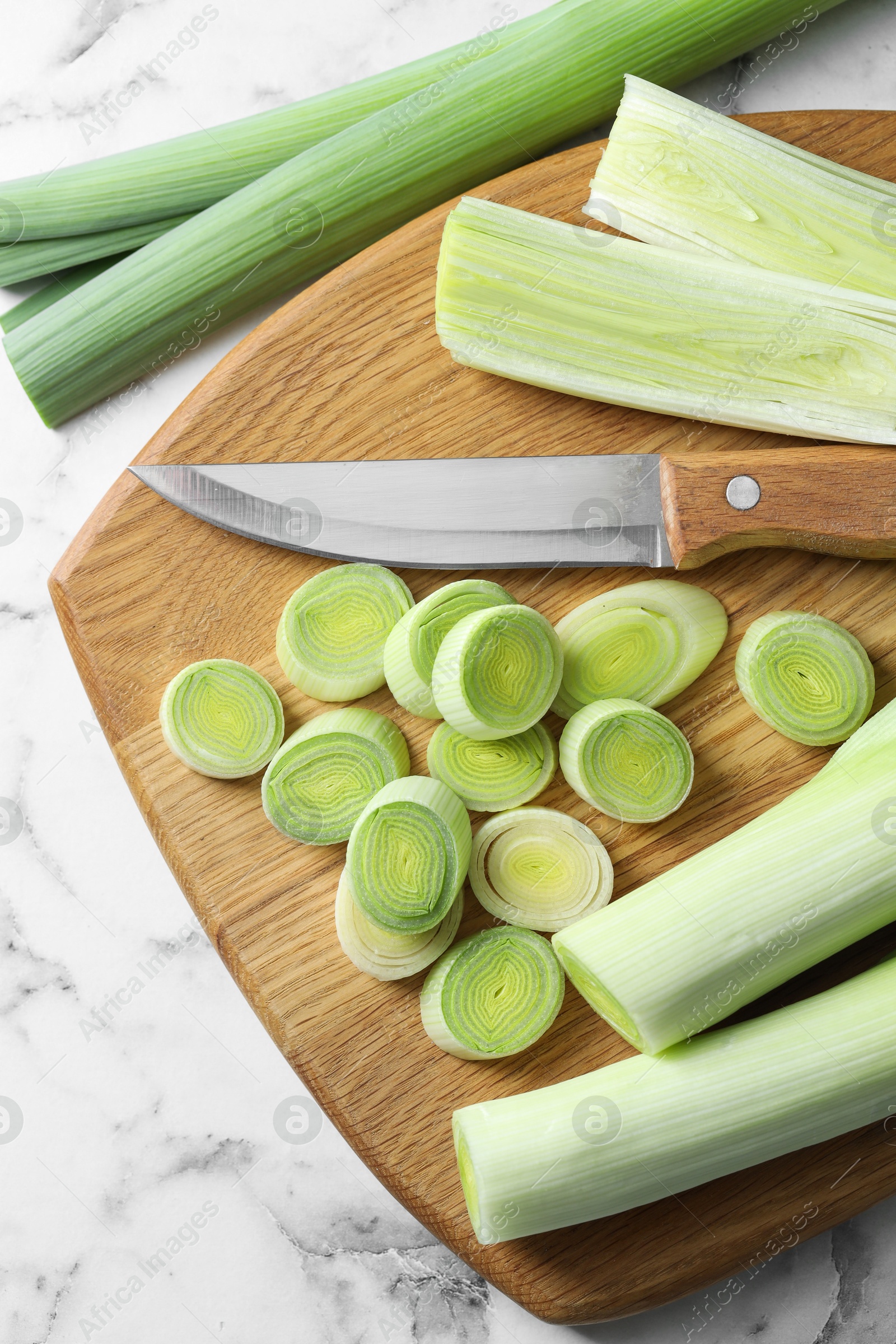 Photo of Chopped leeks, knife and board on white marble table, flat lay