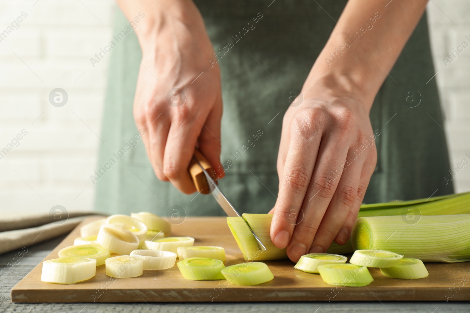 Photo of Woman cutting fresh leek at grey wooden table, closeup