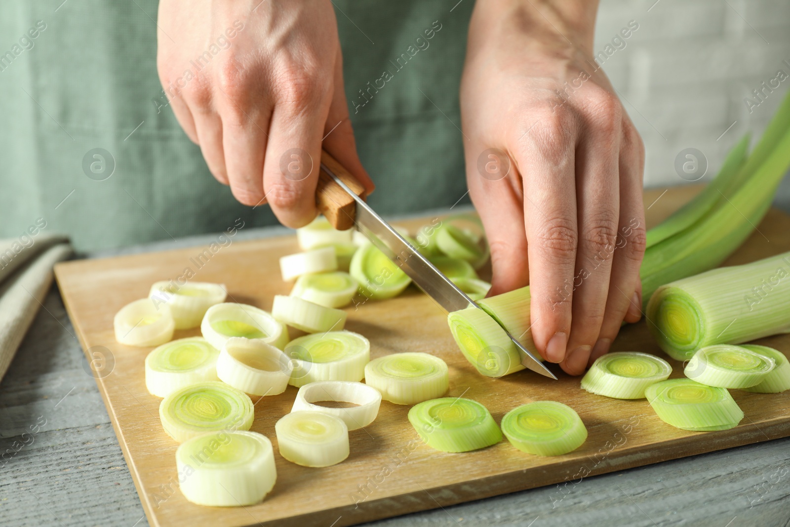 Photo of Woman cutting fresh leek at grey wooden table, closeup