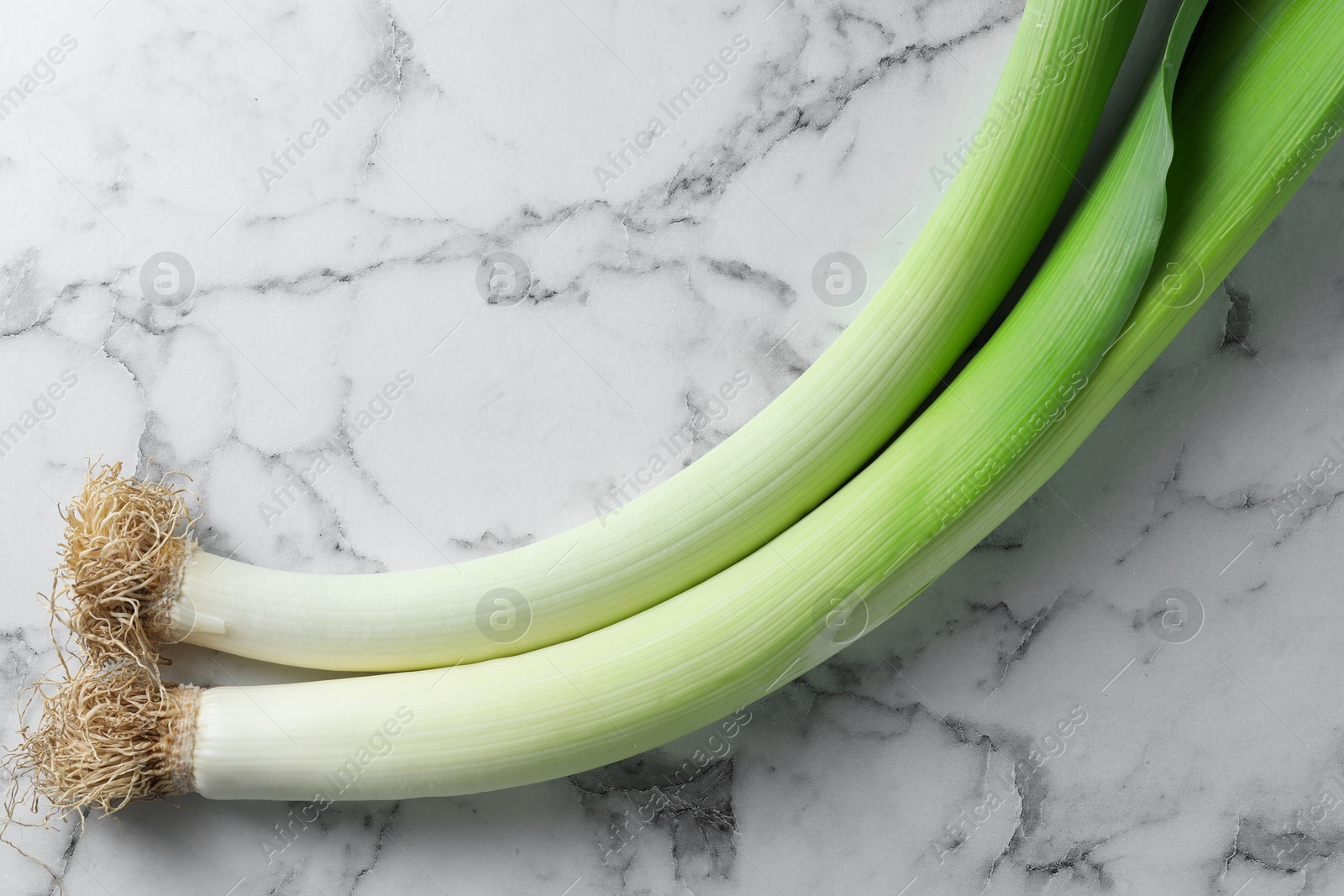 Photo of Whole fresh leeks on white marble table, top view. Space for text