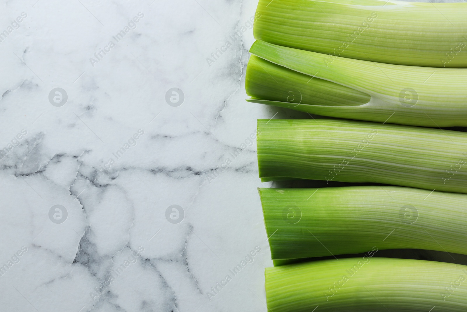 Photo of Whole fresh leeks on white marble table, top view. Space for text