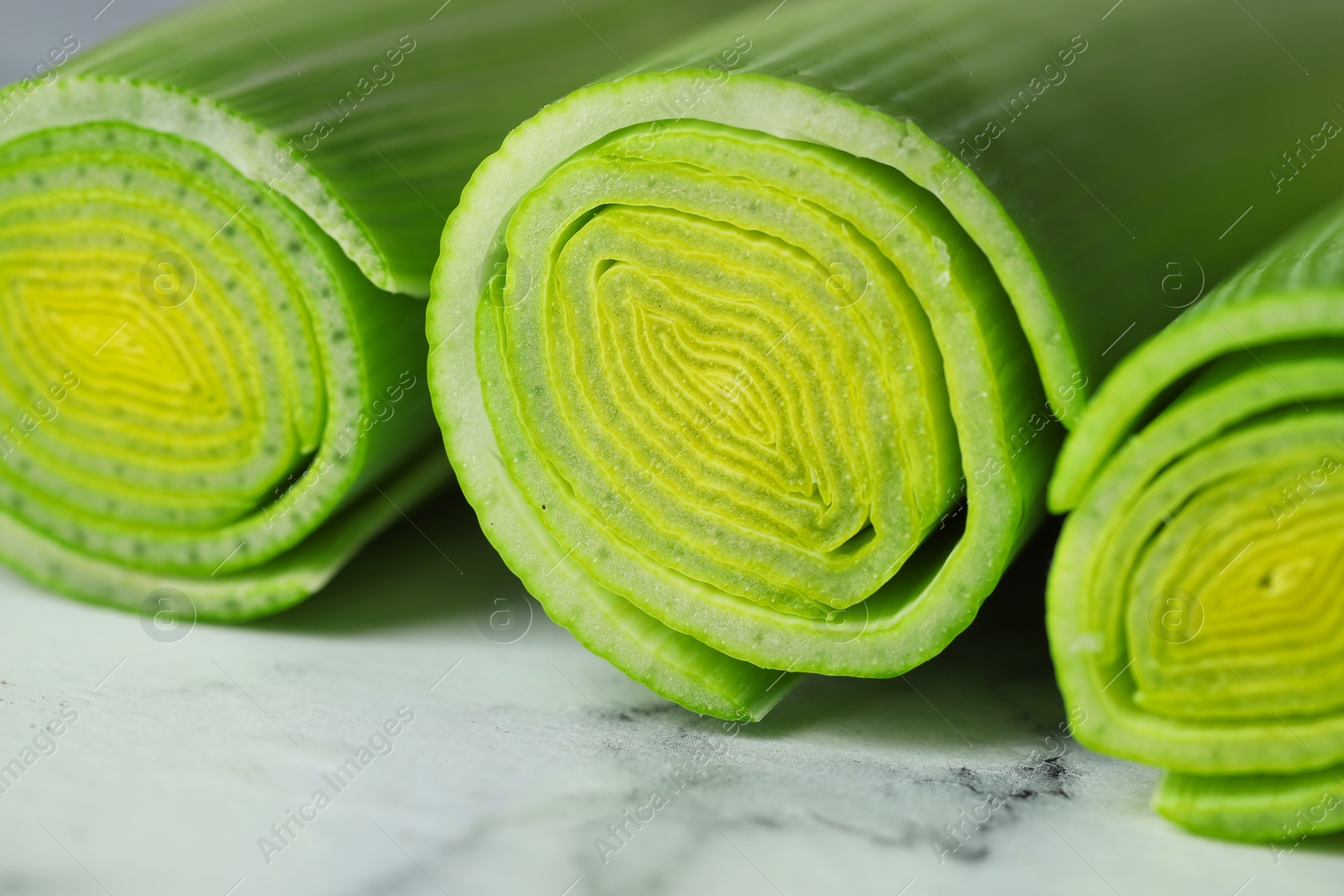 Photo of Whole fresh leeks on white marble table, closeup