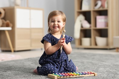 Photo of Cute little girl playing with toy xylophone on floor at home