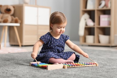 Photo of Cute little girl playing with toy xylophones on floor at home