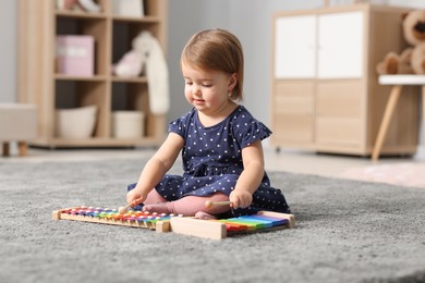 Photo of Cute little girl playing with toy xylophones on floor at home