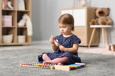 Photo of Cute little girl playing with toy xylophones on floor at home