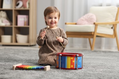 Photo of Cute little girl playing with toy musical instruments on floor at home