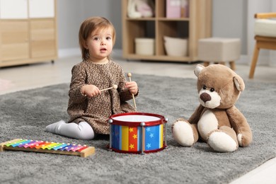 Photo of Cute little girl playing with toy musical instruments on floor at home