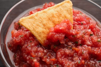 Spicy salsa sauce in glass bowl and nacho chip on table, closeup