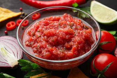 Photo of Spicy salsa sauce in bowl and ingredients on table, closeup