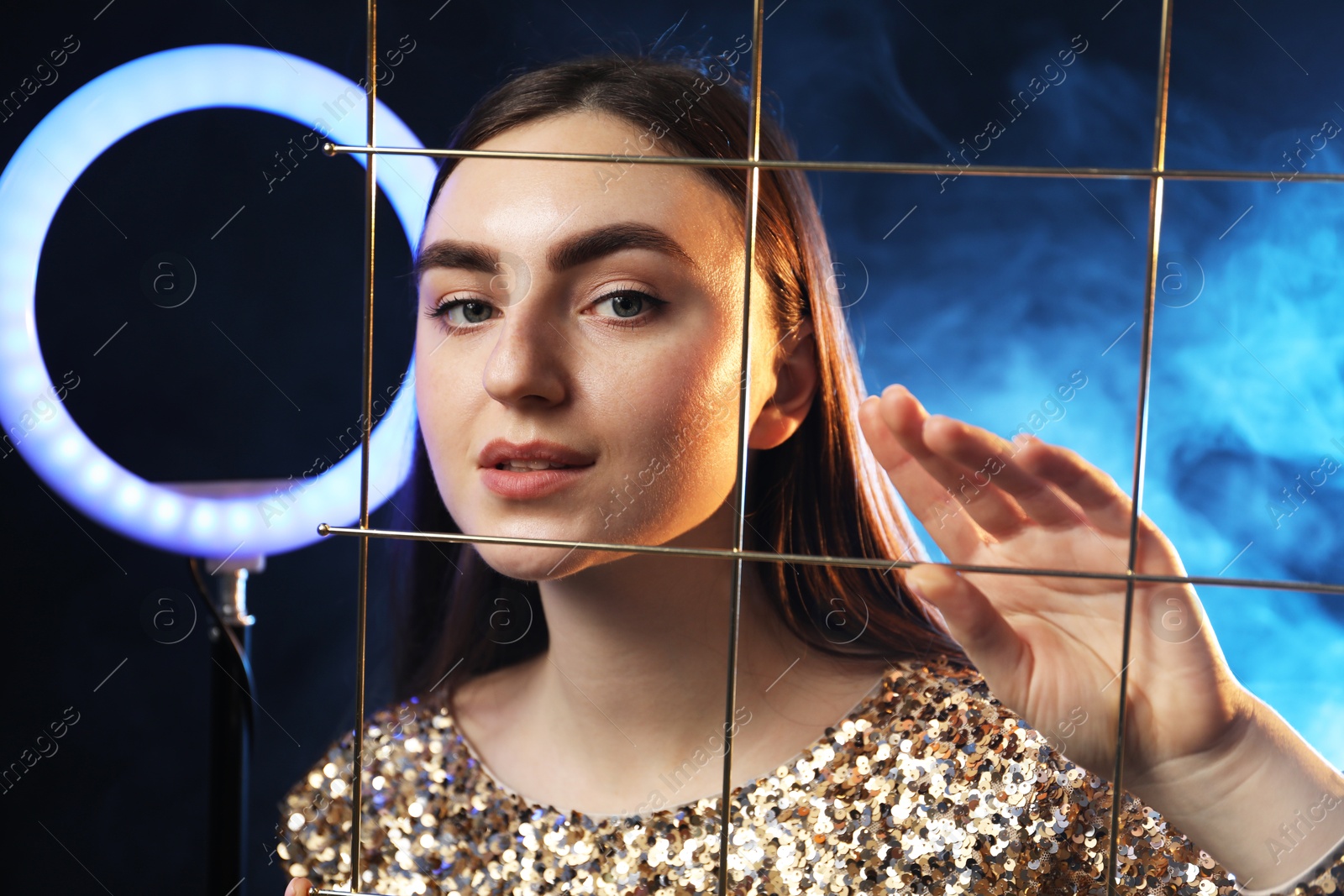 Photo of Beautiful woman with grid and ring lamp on dark blue background in smoke