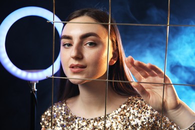 Photo of Beautiful woman with grid and ring lamp on dark blue background in smoke